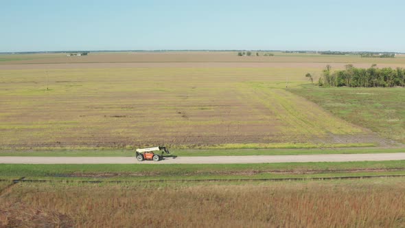 Aerial, skid steer front loader driving on countryside farm road