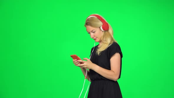 Cheerful Girl Walks in Big Red Headphones and with a Smartphone, Switches Music and Dancing. Chroma