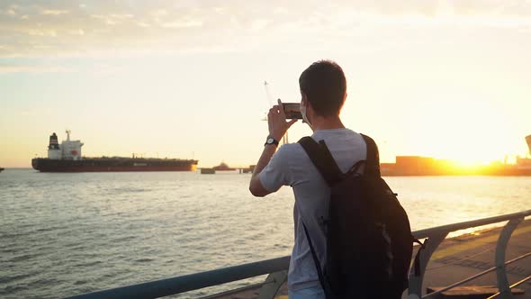 Man With Backpack Taking Photo Of A Ship Moored At Quiet Ocean At The Port Of Puerto Ingeniero White