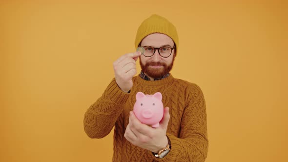 Smiling Millennial Caucasian Hipster Man Putting Money to His Piggy Bank Yellow Studio Background