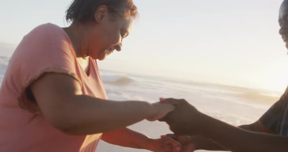 Smiling senior african american couple holding hands and dancing on sunny beach