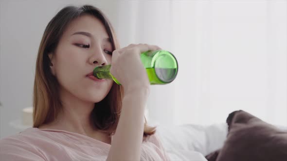 Asian woman drinking beer and watching TV sitting on a couch in the living room at home.