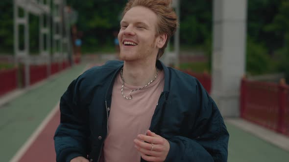 Carefree Young Man with Red Hair Running on City Bridge