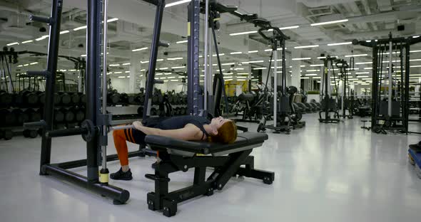 Athletic Girl in the Gym Doing Lying Exercises on Her Legs with a Barbell, Raises and Lowers the