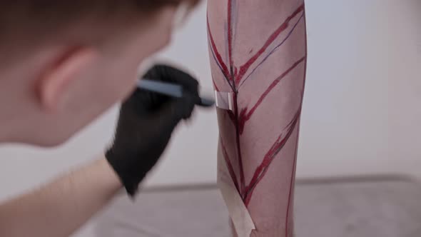 Young Man Tattoo Artist Drawing a Sketch on the Leg on His Client with a Pen