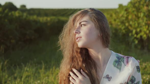 Young Lady with Long Hair and Wore in Dress Sits in Pose and Looks Aside