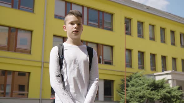 A Caucasian Teenage Boy Talks to the Camera  View From Below  a School in the Background