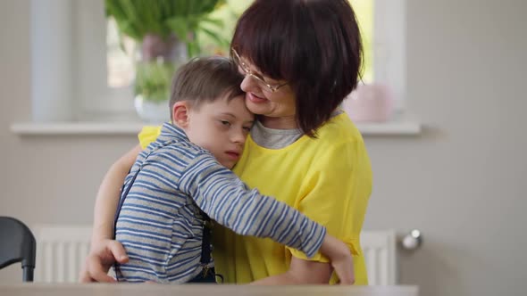 Loving Autistic Son Hugging Mother Sitting with Parent at Table Indoors