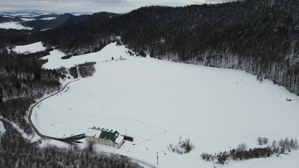 Mountain plateau covered with snow. Forest, clouds and building are in this aerial shot.