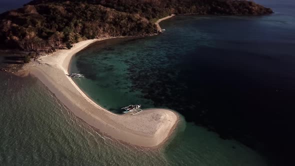 Beautiful tropical island sandbar, curved beach, turquoise sea, waves and boats. Aerial drone view.