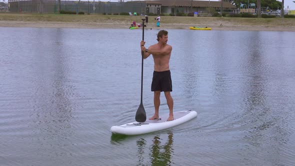 A man paddles his SUP stand-up paddleboard in a lake.