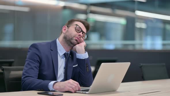 Middle Aged Businessman with Laptop Taking Nap at Work