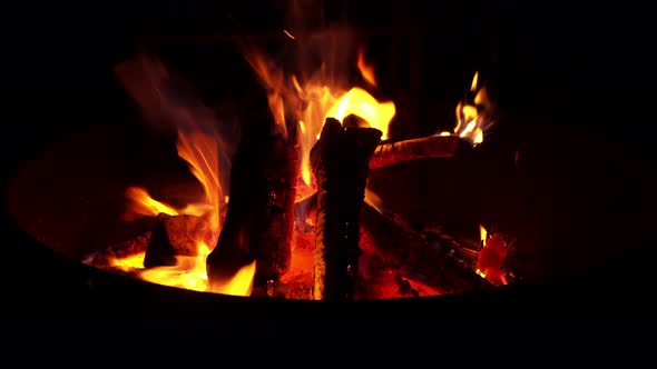 Campfire flames burn firewood bright orange during night at outdoor campsite.