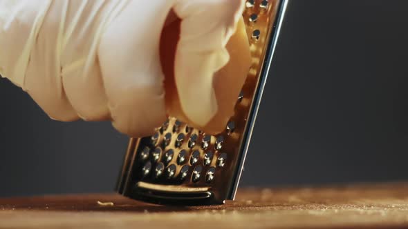 Chef in Gloves Grates Delicious Cheese Lump on Wooden Board