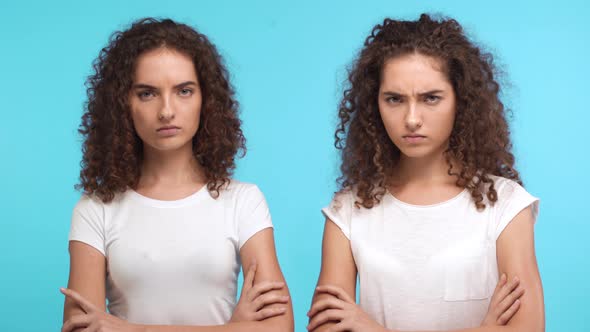 Two Grumpy Resentful Young Caucasian Female Twins in White Tshirts Standing Close to Each Other with