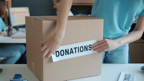 Closeup of Hand Sticking Donation Label Onto Cardboard Box in Charity Organization