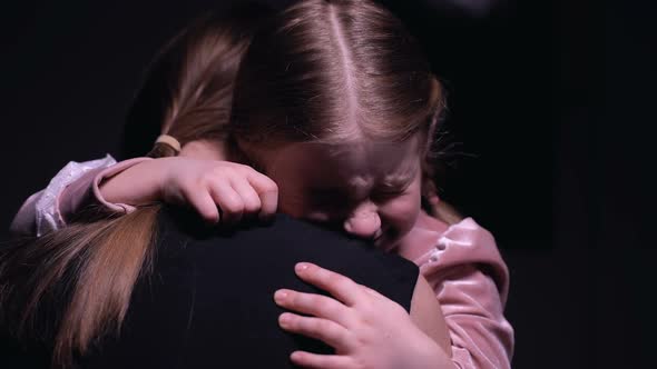 Frightened Girl Hugging Mother and Crying Against Black Background Consternation