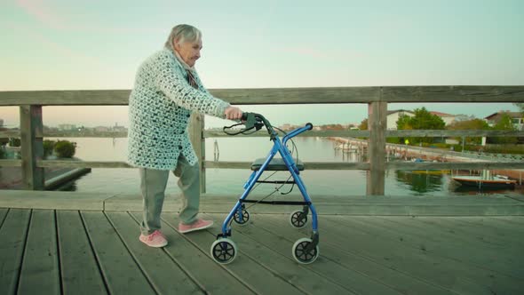 Old Woman Walks on Bridge Over Lagoon with Wheelchair