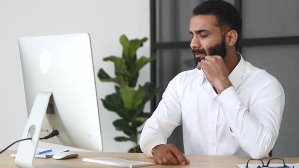 Overworked Frustrated Indian Businessman Manager Sitting at a Desk in the Office Massaging His Neck