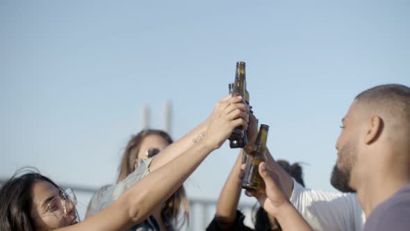 Happy People Clinking Beer Bottles Against Blue Sky.