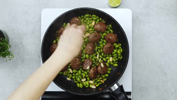 Woman adding peanuts to meatballs with beans