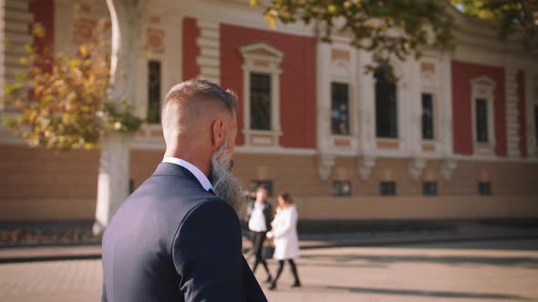 Handsome Bearded Mature Man in Suit Walking Outdoors on Modern Building Background During Sunny Day