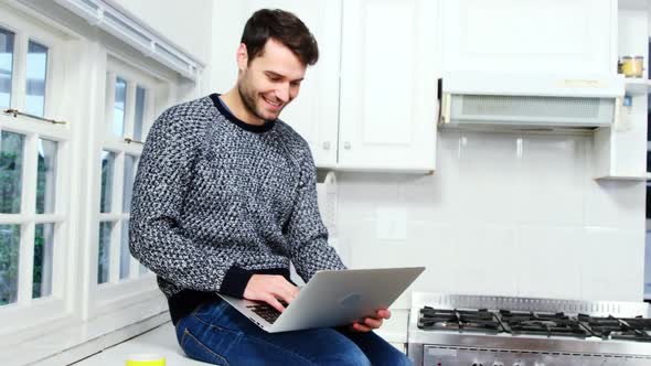 Man using laptop while having coffee in kitchen