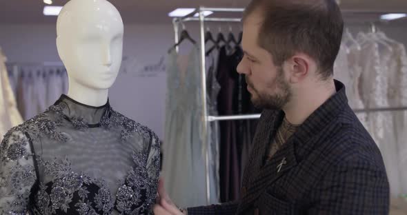 Tailor Corrects Sewn Dress on a Mannequin and Looks at Camera with Crossed Hands