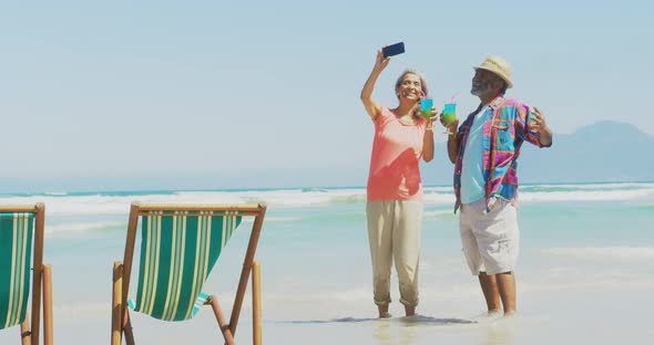 Front view of active senior African American couple taking selfie with mobile phone on the beach 4k