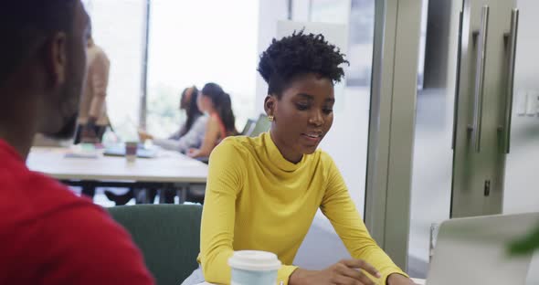 African american male and female business colleagues talking and using laptop in office