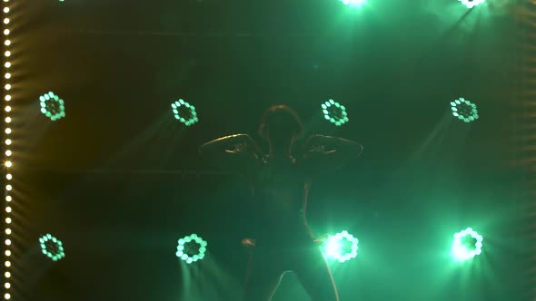 Silhouette of Dancing Young Women on Stage in a Dark Studio with Smoke and Neon Lighting. Green Neon