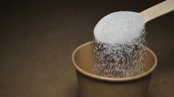 Closeup of Pouring a Full Spoonful of White Sugar Crystals in Slow Motion