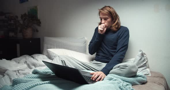 Unwell Feeling Freelance Man Sitting on Sofa Coughs and Working with Computer