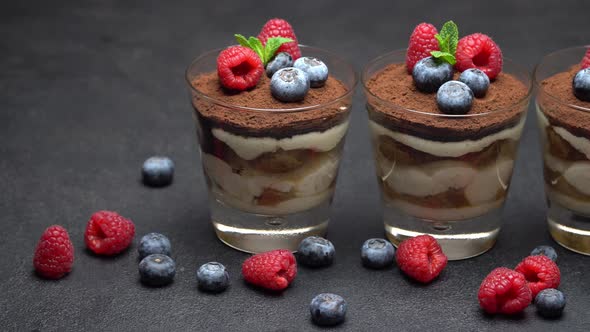Classic Tiramisu Dessert with Blueberries and Raspberries in a Glass on Dark Concrete Background