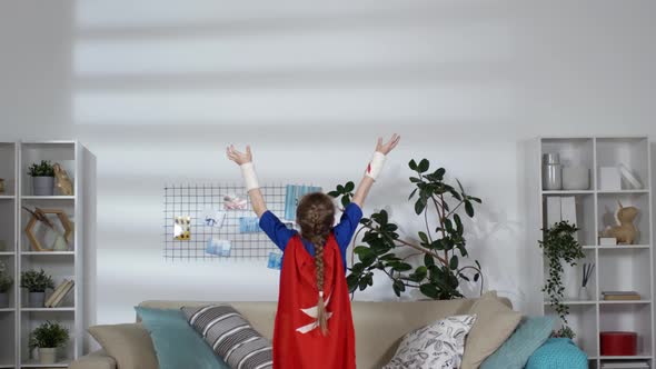 Little Girl in Superhero Costume Holding Arms Raised in Kids Room alt