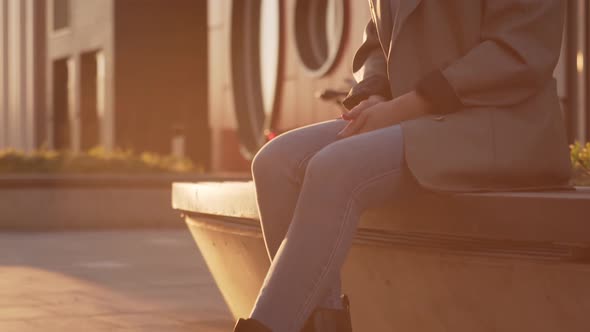 Young attractive business woman sitting outdoor on the bench. Sunset light.