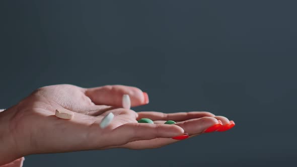 Pills of Different Colours Fall Into Hand with Red Manicure