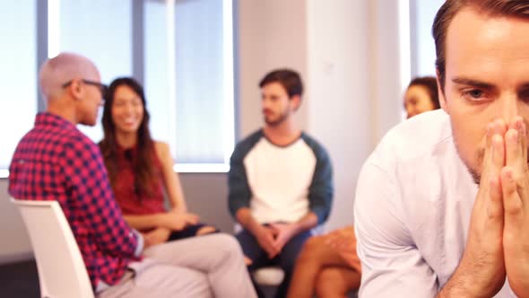 Upset man sitting on chair with colleagues discussing in background