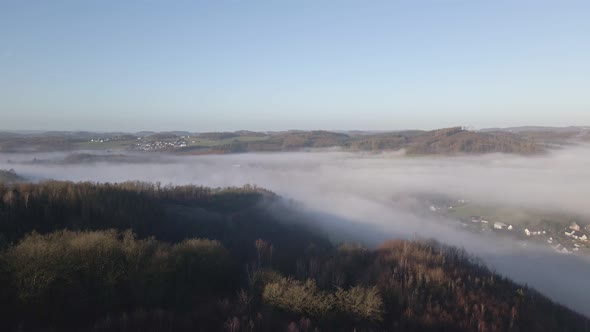 A German village covered completely by a thick layer of fog at sunrise. Aerial tracking shot