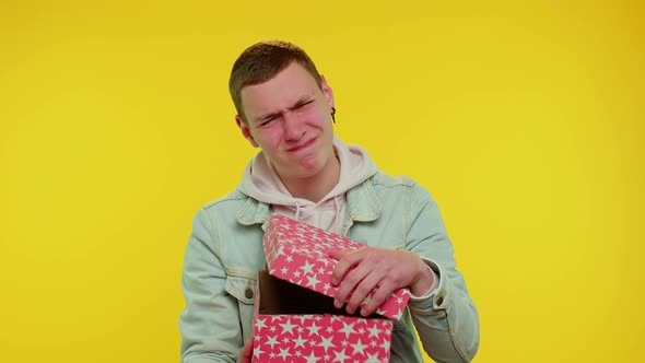 Young Man Unwrapping Birthday Gift and Expressing Disappointment Dislike Bad Present Dissatisfied