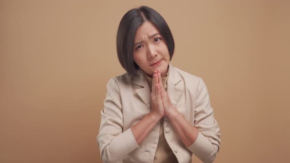 Asian business woman holding hands in prayer looking at camera isolated