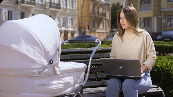 Busy Young Female Trying to Work Laptop and Swinging Newborn in Pram, Child Care