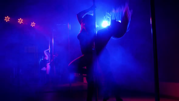 Two Women Dancing Around the Pole By the Light of Colorful Lights