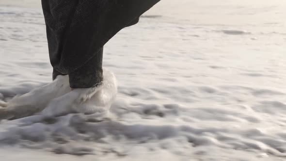 Close up of foamy sea waves splashing female feet at the beach. Woman legs in sea waves.