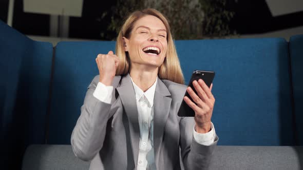 Happy Businesswoman Celebrating Online Victory Lottery on a Mobile Phone Winner