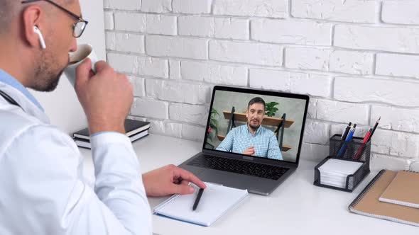 Doctor in Hospital Office Listen Patient Online Video Call Laptop Drinks Coffee