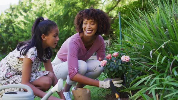 Happy african american mother and daughter, taking care of plants outdoors