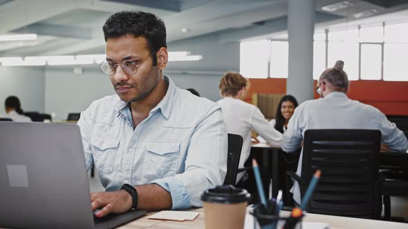 Indian Man Employee Working at Laptop on New Business Project Sitting at Table in Modern Office