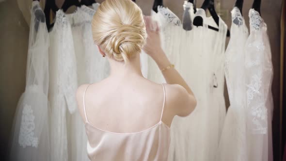 Back View of Young Blond Caucasian Woman Choosing Dress in Boutique. Stylish Beautiful Lady Standing