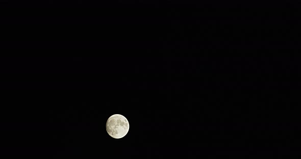 Time-lapse wide shot of a full moon as it rapidly rises from the lower left to the upper right.